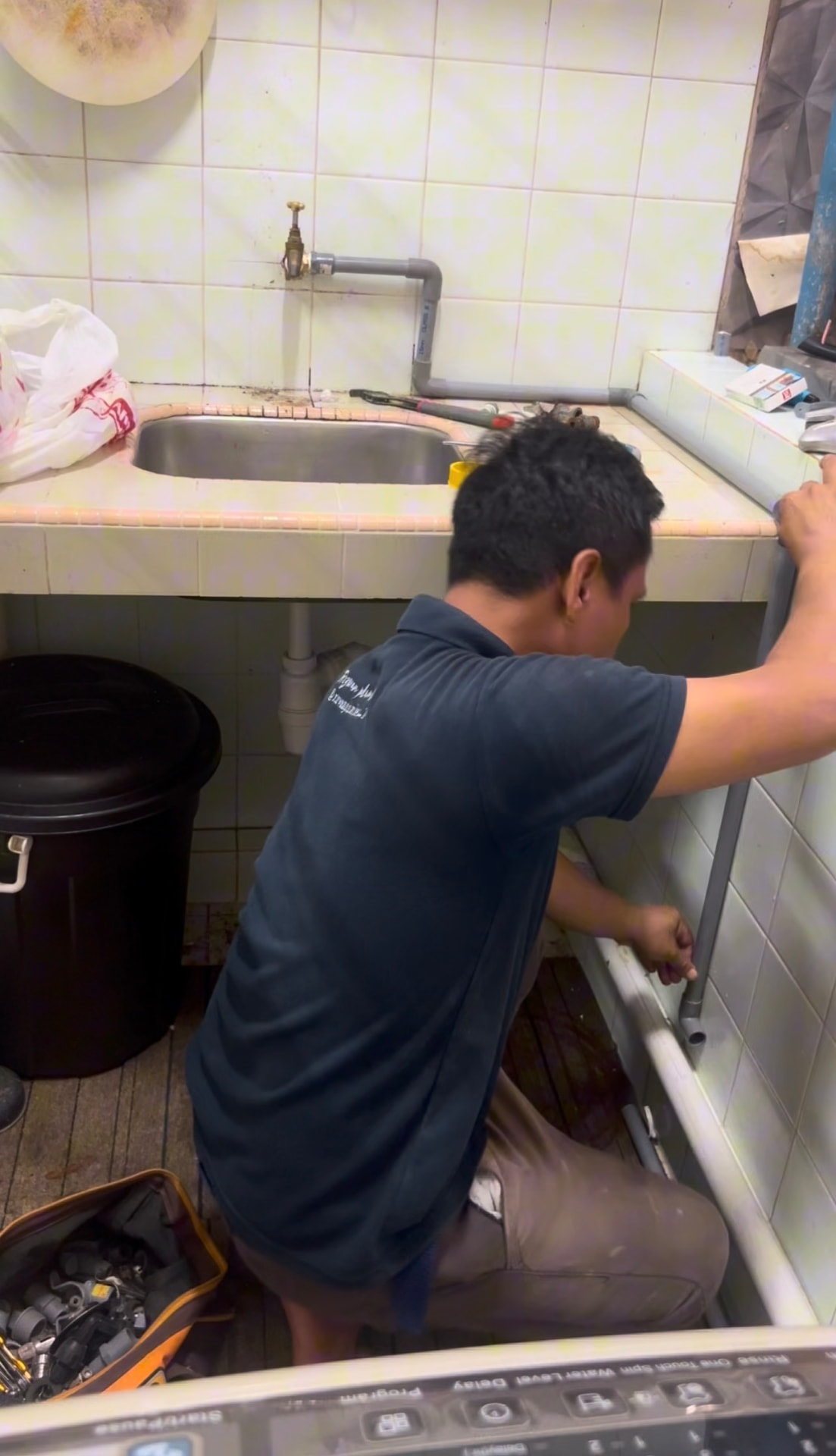 Rizwan sedang membaiki paip di bawah sinki dapur pelanggan